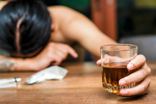 A person laying their head in arm holding a glass of whisky
