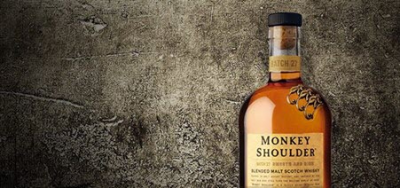 A bottle of Monkey Shoulder blended malt whisky, with a mottled grey backdrop